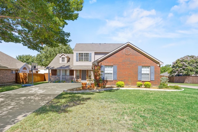 traditional home featuring a front lawn, fence, covered porch, brick siding, and driveway