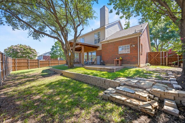 rear view of property featuring brick siding, a fenced backyard, a chimney, a patio area, and a yard