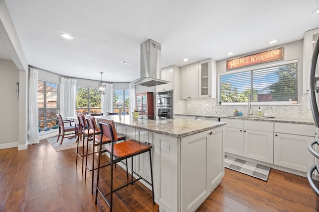 kitchen featuring a sink, stainless steel appliances, island range hood, a kitchen bar, and a kitchen island