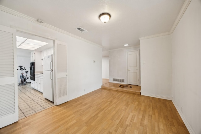 spare room featuring light wood-style floors, baseboards, crown molding, and visible vents