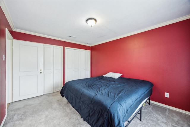 carpeted bedroom featuring crown molding, baseboards, two closets, and visible vents