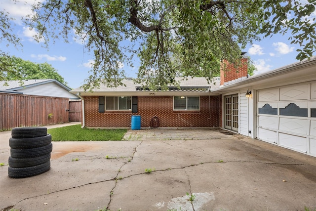 rear view of house featuring a chimney, a garage, brick siding, fence, and concrete driveway