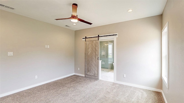 spare room featuring a ceiling fan, visible vents, a barn door, baseboards, and carpet