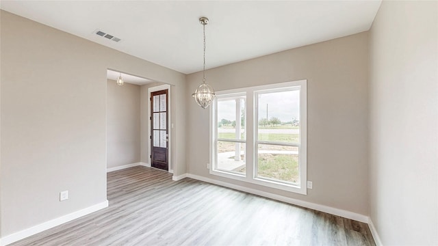 unfurnished dining area featuring visible vents, baseboards, wood finished floors, and an inviting chandelier