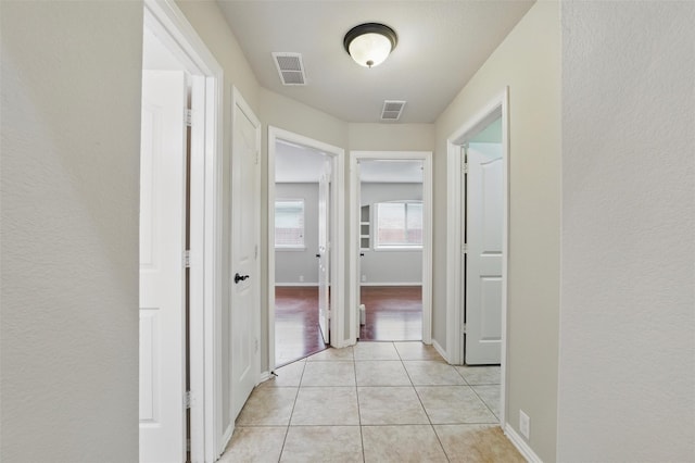 hall with light tile patterned floors, baseboards, and visible vents