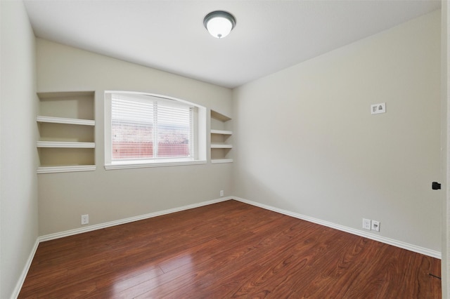 unfurnished room with baseboards, dark wood-style flooring, and built in shelves