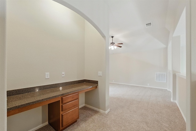unfurnished office featuring visible vents, arched walkways, built in desk, and light carpet