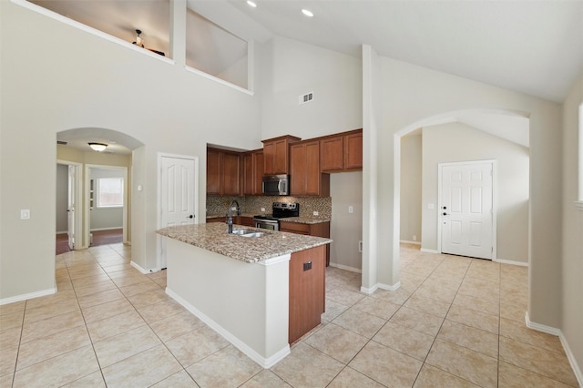 kitchen with arched walkways, appliances with stainless steel finishes, a sink, light stone counters, and light tile patterned flooring