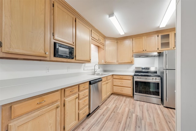 kitchen featuring appliances with stainless steel finishes, a sink, light brown cabinets, light wood-style flooring, and under cabinet range hood