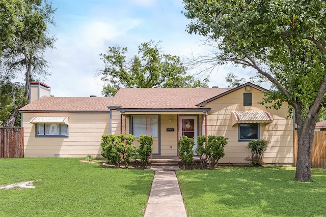 ranch-style home featuring a shingled roof, a front lawn, fence, and a chimney
