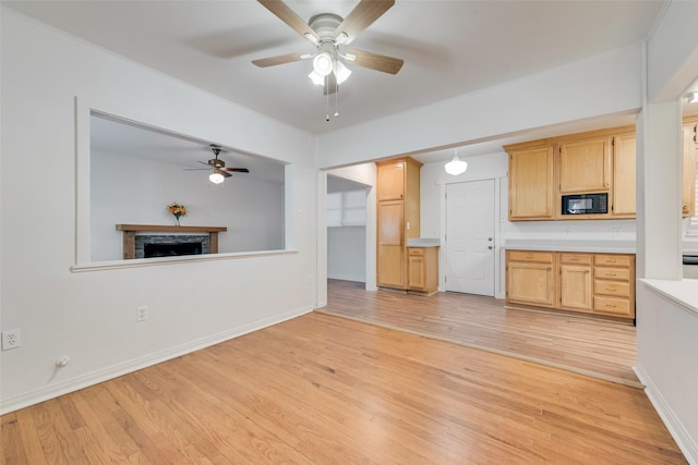 unfurnished living room with a ceiling fan, baseboards, light wood-style flooring, and a fireplace