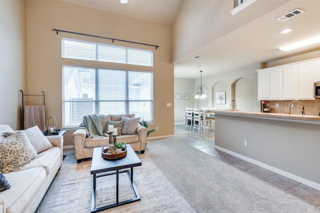 living room featuring a high ceiling, light carpet, arched walkways, baseboards, and visible vents