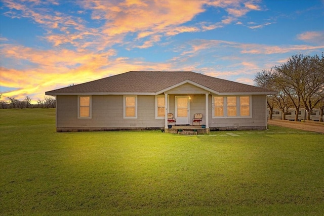 back of house at dusk with a lawn and a shingled roof