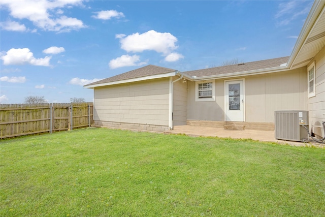 rear view of house with fence, cooling unit, a shingled roof, a patio area, and a lawn