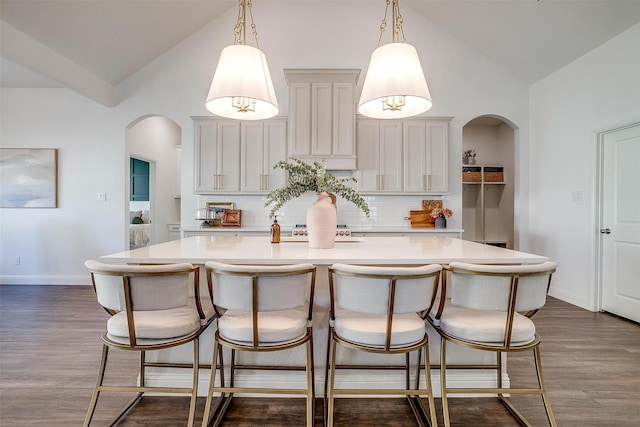 kitchen with light countertops, arched walkways, decorative backsplash, and high vaulted ceiling
