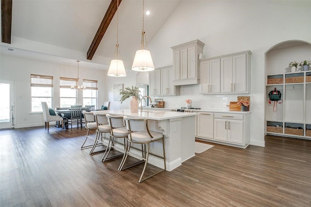 kitchen featuring light countertops, a kitchen island with sink, high vaulted ceiling, a breakfast bar area, and dark wood-type flooring