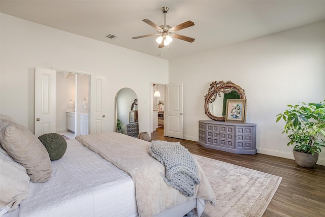 bedroom featuring visible vents, wood finished floors, baseboards, arched walkways, and ensuite bath