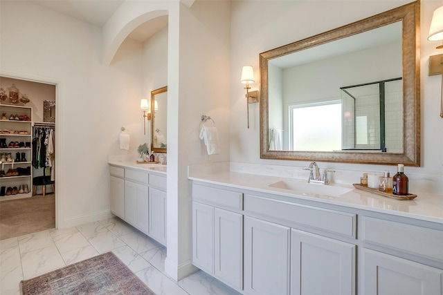 full bathroom featuring a sink, marble finish floor, two vanities, a spacious closet, and a stall shower
