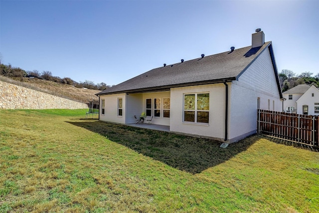 back of property with fence, roof with shingles, a chimney, brick siding, and a yard