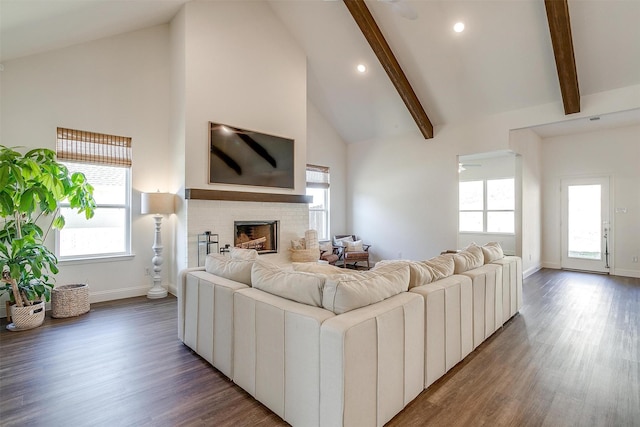 living area with baseboards, beam ceiling, a brick fireplace, and wood finished floors