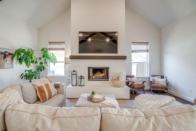 living area with baseboards, a fireplace with raised hearth, wood finished floors, and high vaulted ceiling
