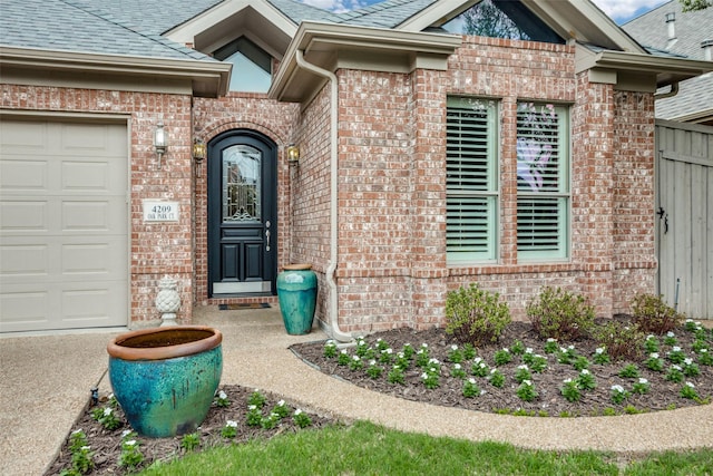 doorway to property with brick siding, an attached garage, fence, and a shingled roof