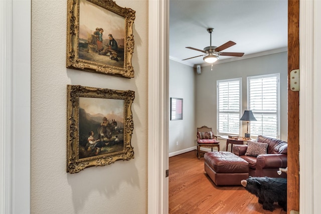 sitting room with crown molding, a ceiling fan, baseboards, and wood finished floors