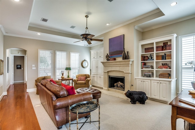 living room featuring crown molding, ceiling fan, arched walkways, a premium fireplace, and visible vents