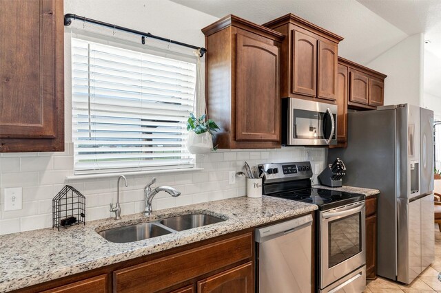 kitchen with light stone counters, a sink, decorative backsplash, and stainless steel appliances