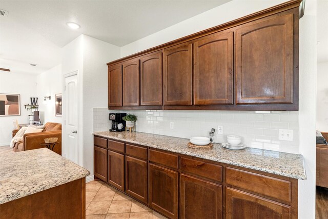 kitchen with open floor plan, backsplash, light tile patterned flooring, and light stone countertops