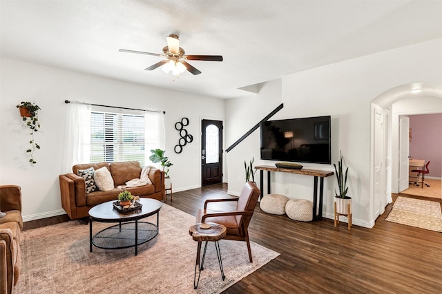 living area with baseboards, arched walkways, ceiling fan, and dark wood-style floors