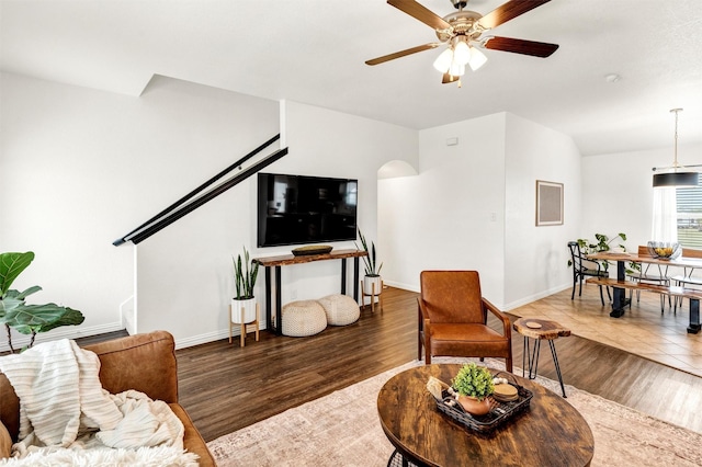 living area with baseboards, arched walkways, ceiling fan, and wood finished floors