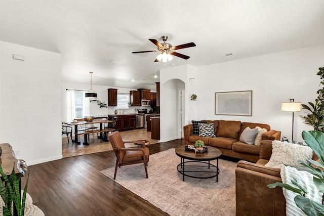 living room featuring arched walkways, a ceiling fan, dark wood-style floors, and visible vents