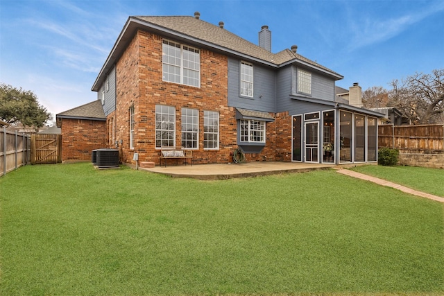 back of house with brick siding, a sunroom, a fenced backyard, a chimney, and a patio