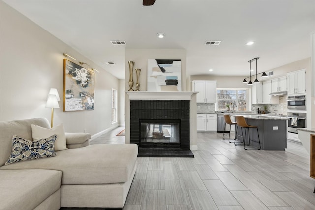 living area featuring a brick fireplace, recessed lighting, ceiling fan, and visible vents