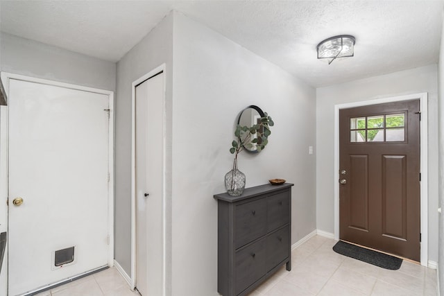entryway with light tile patterned floors, baseboards, and a textured ceiling