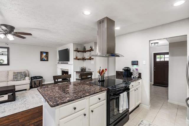 kitchen featuring a peninsula, black electric range oven, island range hood, white cabinetry, and a ceiling fan