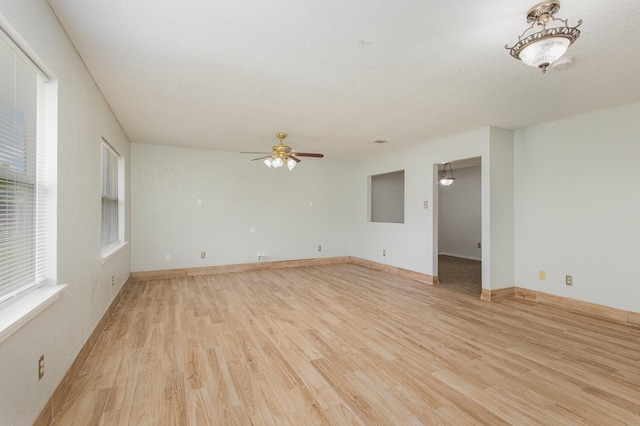 empty room featuring light wood-style floors, baseboards, ceiling fan, and a healthy amount of sunlight