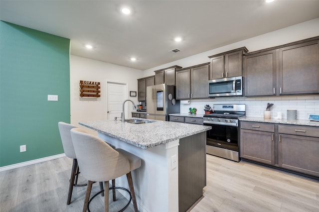 1529 Babb Ln, Celina, TX 75009 - kitchen featuring dark brown cabinets, a breakfast bar, light wood-style floors, stainless steel appliances, and a center island with sink