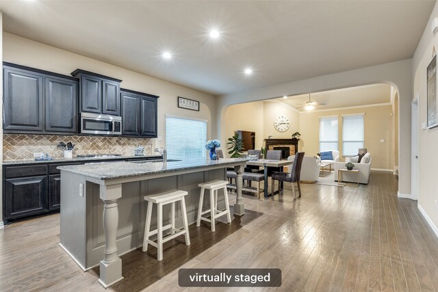 kitchen featuring a sink, an island with sink, a kitchen breakfast bar, arched walkways, and stainless steel appliances