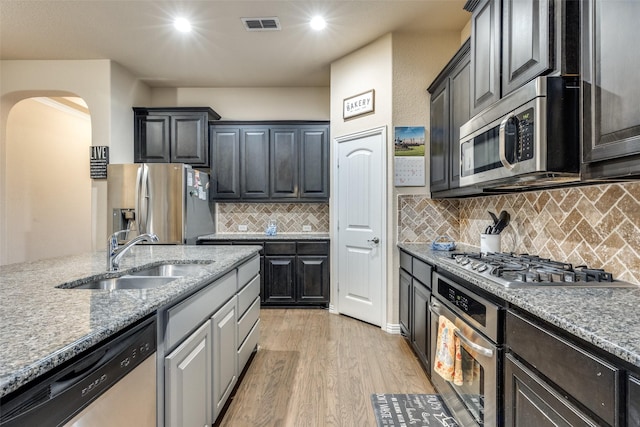 kitchen featuring visible vents, a sink, light stone counters, arched walkways, and stainless steel appliances