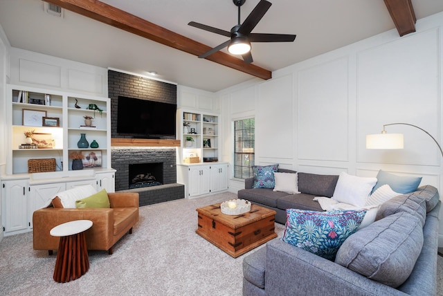 carpeted living area with visible vents, a brick fireplace, a decorative wall, beamed ceiling, and a ceiling fan