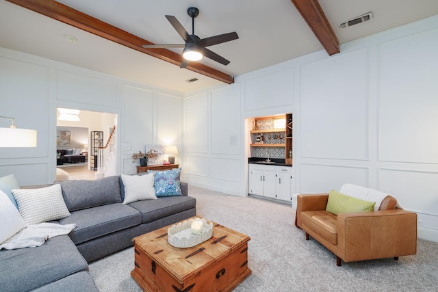 living room with a ceiling fan, a decorative wall, beam ceiling, and visible vents