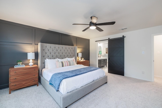 bedroom featuring ceiling fan, visible vents, a barn door, light carpet, and ensuite bath
