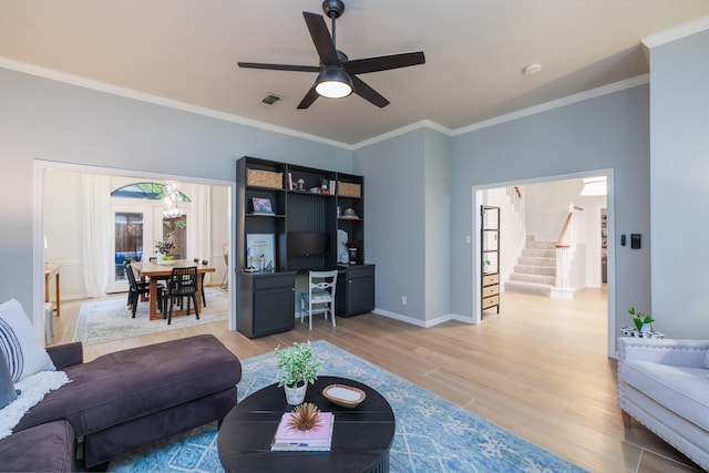 living room featuring a ceiling fan, ornamental molding, stairway, and light wood-style floors