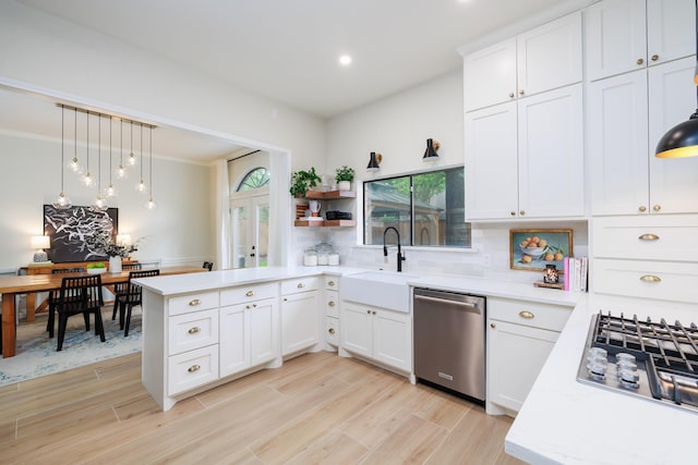 kitchen featuring hanging light fixtures, a sink, a peninsula, stainless steel appliances, and white cabinetry