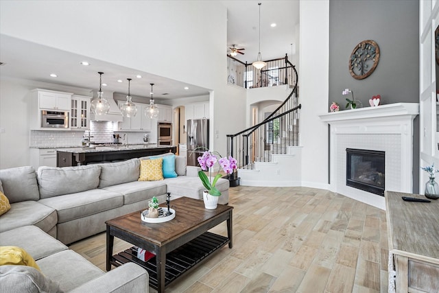 living area featuring ceiling fan, light wood-style floors, a glass covered fireplace, stairs, and recessed lighting
