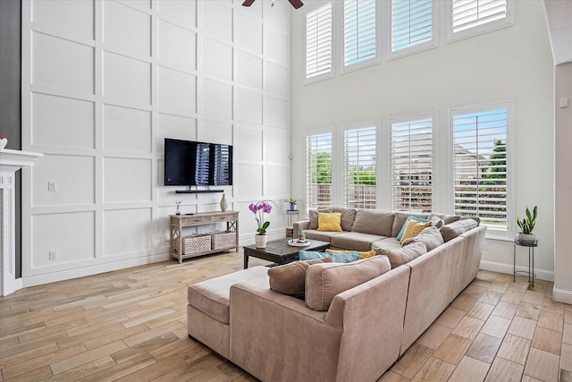 living area with plenty of natural light, ceiling fan, light wood finished floors, a high ceiling, and a decorative wall
