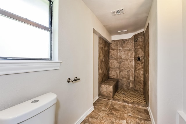 bathroom featuring toilet, baseboards, visible vents, and a tile shower