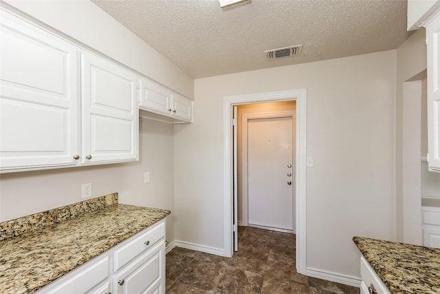 kitchen with white cabinets, baseboards, visible vents, and light stone counters